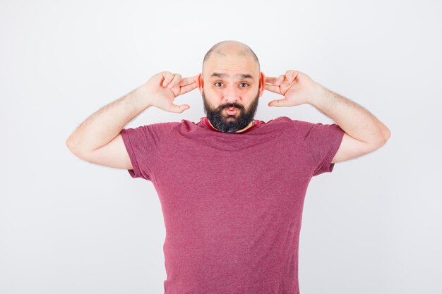 Junge Männer, die Ohren mit den Fingern im rosa T-Shirt berühren und lustig aussehen. Vorderansicht.