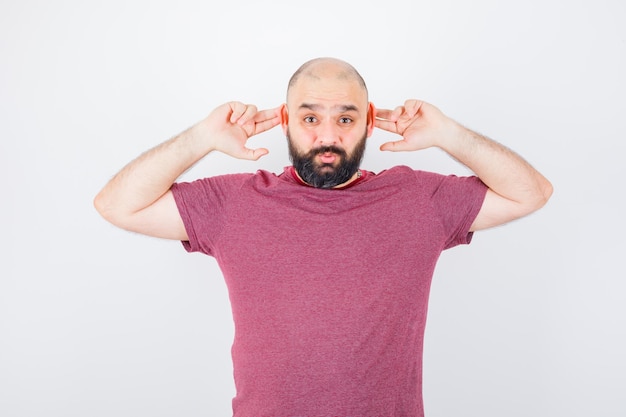 Junge Männer, die Ohren mit den Fingern im rosa T-Shirt berühren und lustig aussehen. Vorderansicht.