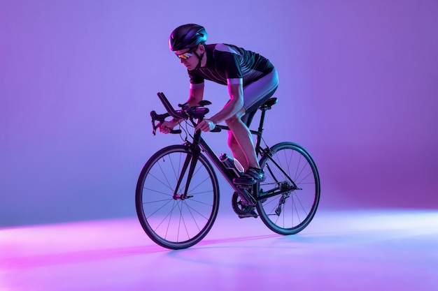 Junge männliche Fahrradfahrer auf dem Fahrrad isoliert auf einer Gradientenwand im Neon-Mann-Training und -Üben