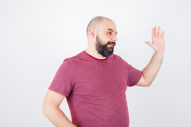 Junge männliche hand winken zur begrüßung in rosa t-shirt und hell aussehend, vorderansicht.