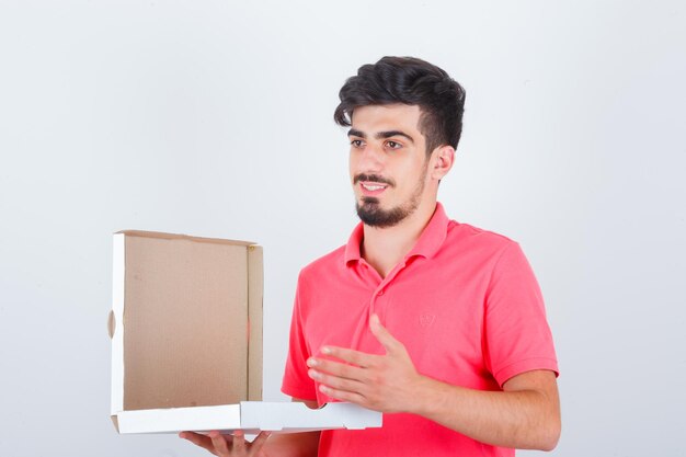 Junge männliche Holding öffnete Pizzakarton im T-Shirt und sieht hübsch aus. Vorderansicht.