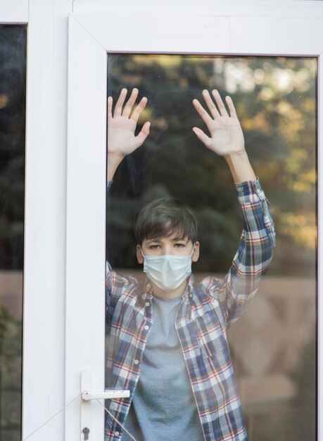 Junge mit der medizinischen Maske, die draußen schaut