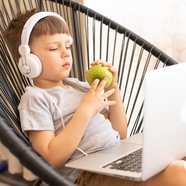Junge mit Kopfhörern und Laptop, der Apfel isst