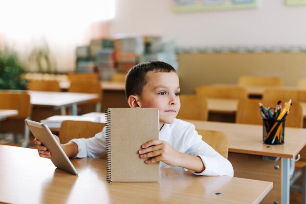 Junge mit Tablette und Notizblock am Tisch