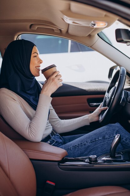 Junge moderne muslimische Frau, die Kaffee im Auto trinkt