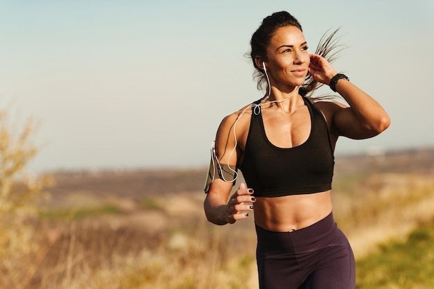 Junge muskulöse Frau, die joggt, während sie Musik über Kopfhörer in der Natur hört Kopieren Sie Platz