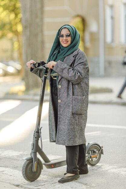 Junge muslimische Frau, die einen Roller auf einer Straße fährt