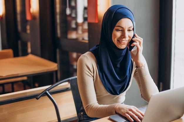 Junge muslimische Frau, die in einem Café telefoniert und am Computer arbeitet?