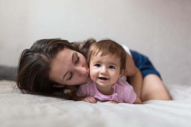 Junge Mutter der glücklichen liebevollen Familie, die mit ihrem Baby im Schlafzimmer spielt