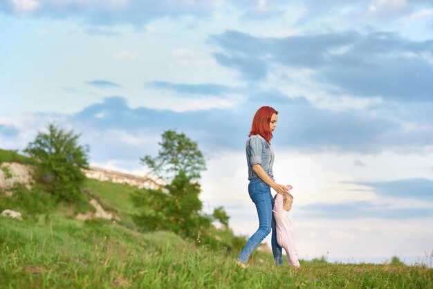 Junge Mutter, die auf dem Feld läuft und die Hände der kleinen Tochter hält