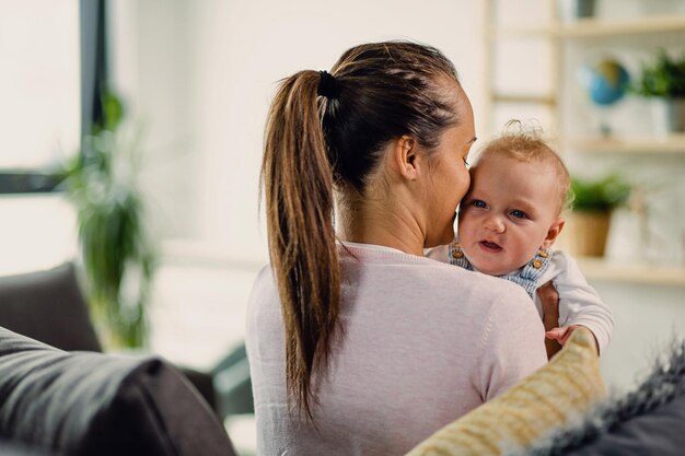 Junge Mutter, die ihren kleinen Jungen hält, während sie Zeit zusammen zu Hause verbringt