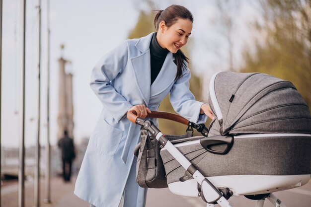 Junge Mutter, die mit Kinderwagen im Park geht