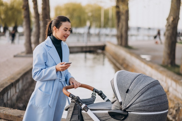 Junge Mutter, die mit Kinderwagen im Park geht