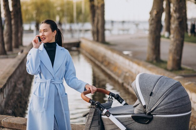 Junge Mutter, die mit Kinderwagen im Park geht