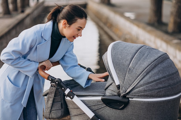 Junge Mutter, die mit Kinderwagen im Park geht