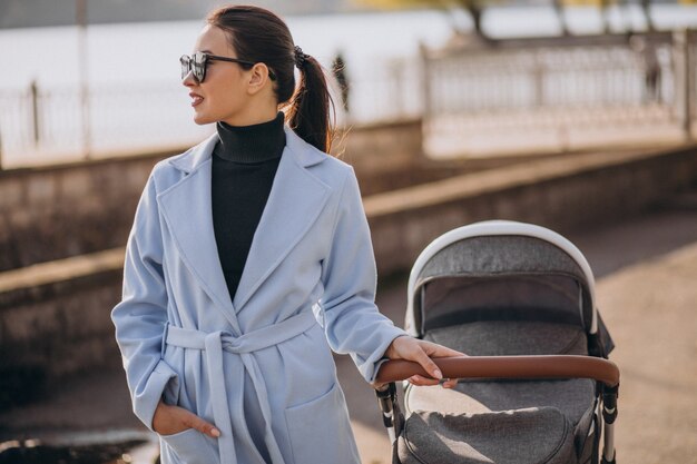 Junge Mutter, die mit Kinderwagen im Park geht