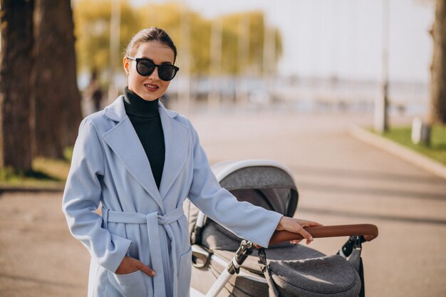 Junge Mutter, die mit Kinderwagen im Park geht