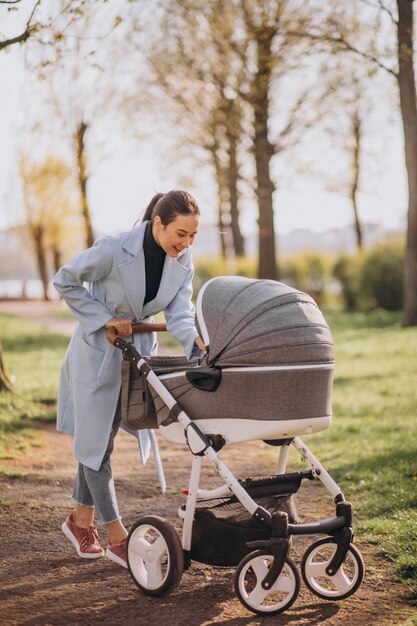 Junge Mutter, die mit Kinderwagen im Park geht