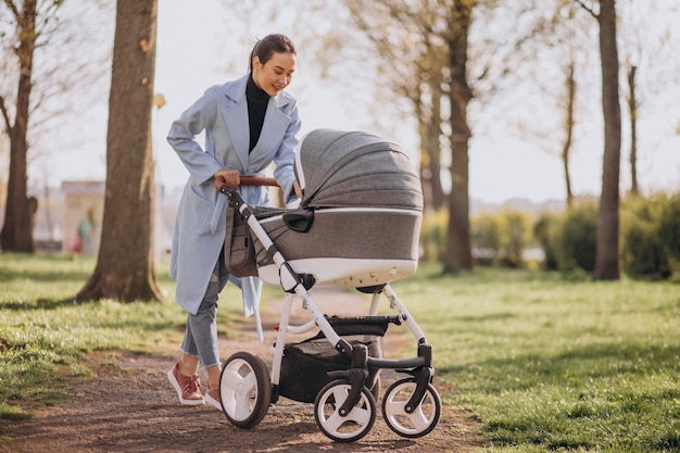 Junge Mutter, die mit Kinderwagen im Park geht