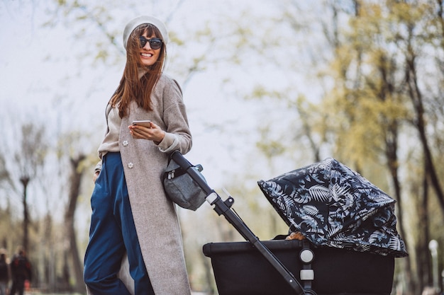 Junge Mutter, die mit Kinderwagen im Park geht