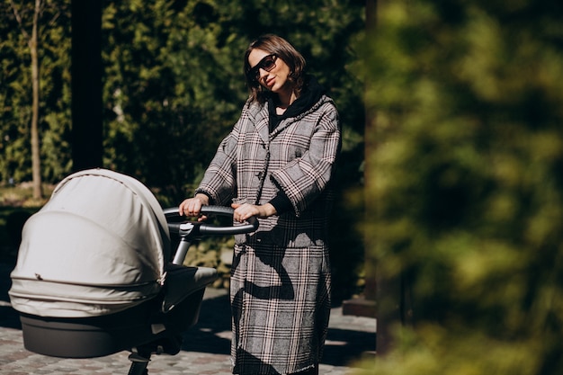 Junge Mutter, die mit Kinderwagen im Park geht