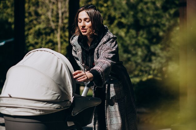 Junge Mutter, die mit Kinderwagen im Park geht