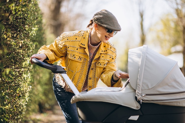 Junge Mutter, die mit Kinderwagen im Park geht