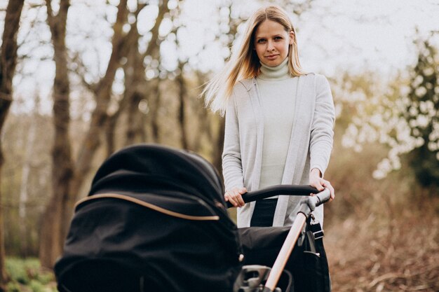 Junge Mutter, die mit Kinderwagen im Park geht