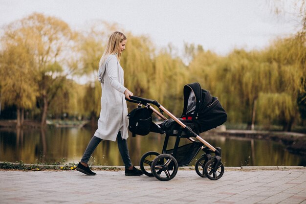 Junge Mutter, die mit Kinderwagen im Park geht