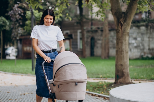 Junge Mutter, die mit Kinderwagen im Park geht