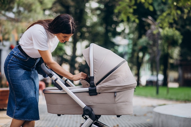 Junge Mutter, die mit Kinderwagen im Park geht