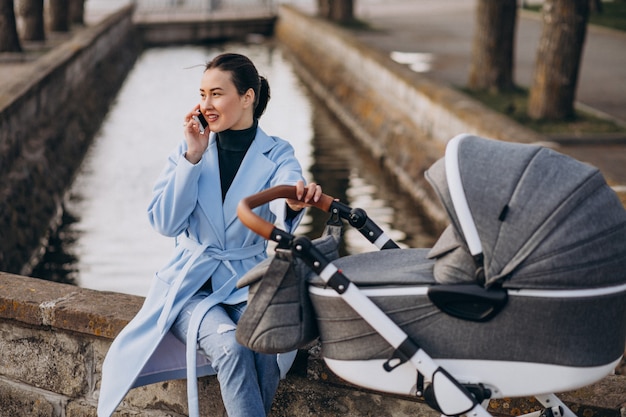 Junge Mutter, die mit Kinderwagen im Park sitzt