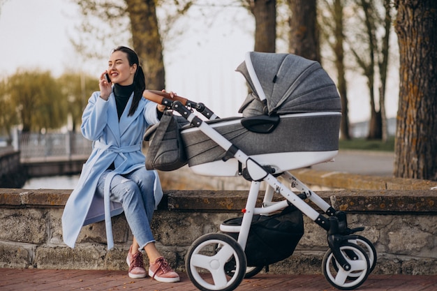 Junge Mutter, die mit Kinderwagen im Park sitzt