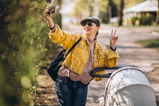 Kostenloses Foto junge mutter, die mit kinderwagen im park und unter verwendung des telefons geht