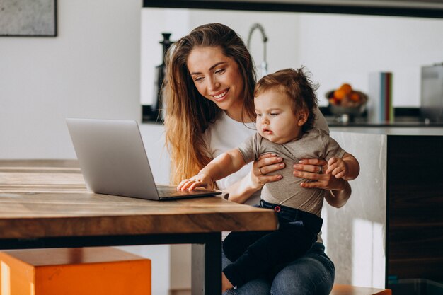 Junge Mutter, die von zu Hause auf Laptop mit ihrem kleinen Sohn arbeitet