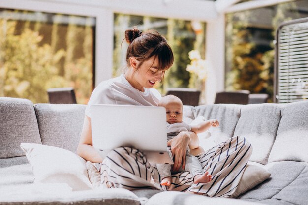 Junge Mutter mit ihrem Kind, das zu Hause an einem Computer arbeitet