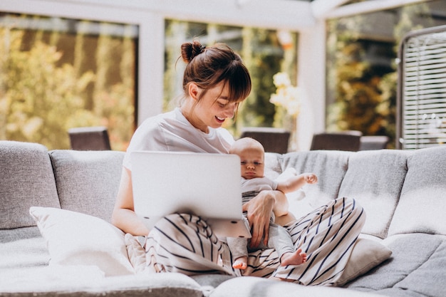 Junge Mutter mit ihrem Kind, das zu Hause an einem Computer arbeitet