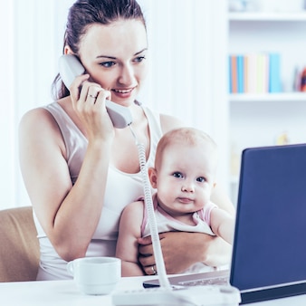 Junge mutter und baby verwenden laptop, um mit oma über skype zu kommunizieren, zu hause im kinderzimmer