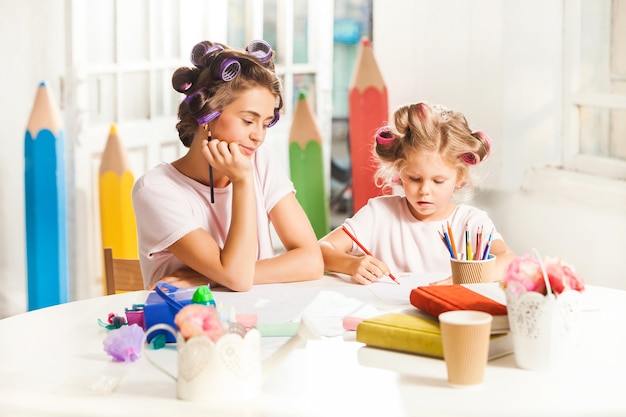 junge Mutter und ihre kleine Tochter zeichnen zu Hause mit Bleistiften