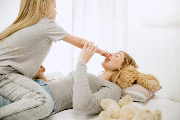 Junge Mutter und ihre kleine Tochter zu Hause am sonnigen Morgen. Weiche Pastellfarben. Glückliche Familienzeit am Wochenende. Muttertagskonzept. Konzepte für Familie, Liebe, Lebensstil, Mutterschaft und zarte Momente.