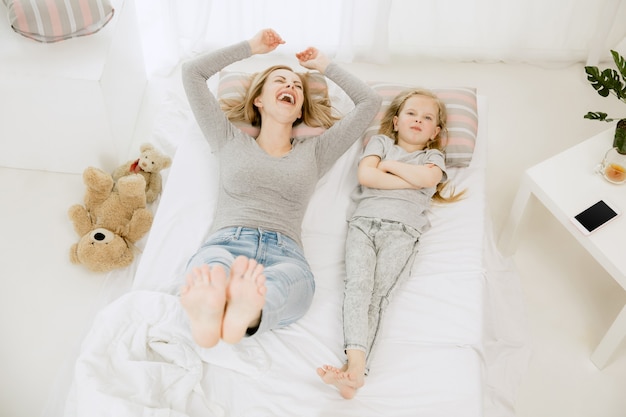 Junge Mutter und ihre kleine Tochter zu Hause am sonnigen Morgen. Weiche Pastellfarben. Glückliche Familienzeit am Wochenende. Muttertagskonzept. Konzepte für Familie, Liebe, Lebensstil, Mutterschaft und zarte Momente.