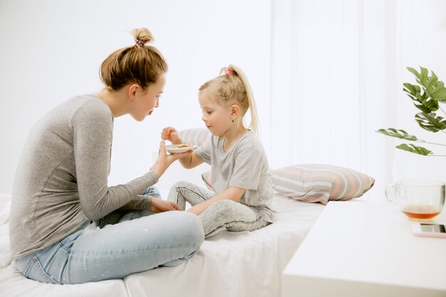 Junge Mutter und ihre kleine Tochter zu Hause am sonnigen Morgen. Weiche Pastellfarben. Glückliche Familienzeit am Wochenende. Muttertagskonzept. Konzepte für Familie, Liebe, Lebensstil, Mutterschaft und zarte Momente.