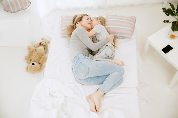 Junge Mutter und ihre kleine Tochter zu Hause am sonnigen Morgen. Weiche Pastellfarben. Glückliche Familienzeit am Wochenende. Muttertagskonzept