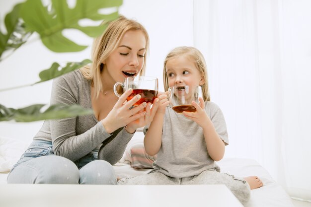 Junge Mutter und ihre kleine Tochter zu Hause am sonnigen Morgen. Weiche Pastellfarben. Glückliche Familienzeit am Wochenende.