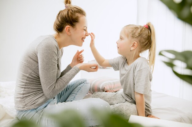 Junge Mutter und ihre kleine Tochter zu Hause am sonnigen Morgen. Weiche Pastellfarben. Glückliche Familienzeit am Wochenende.