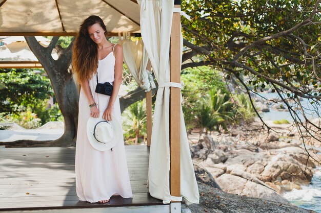 Junge natürliche schöne Frau im blassen Kleid, das im Festzelt, im tropischen Urlaub, im Strohhut, im sinnlichen Sommeroutfit, im Resort, im Boho-Weinlesestil aufwirft