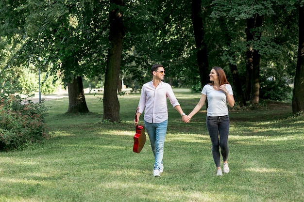 Junge Paare der Totalen, die Hand in Hand durch Wiese gehen