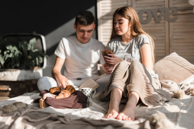 Junge Paare, die auf dem Bett frühstücken sitzen