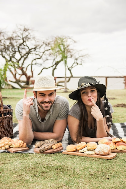 Kostenloses Foto junge paare, die auf dem umfassenden zeigen des fingers auf picknick im park liegen