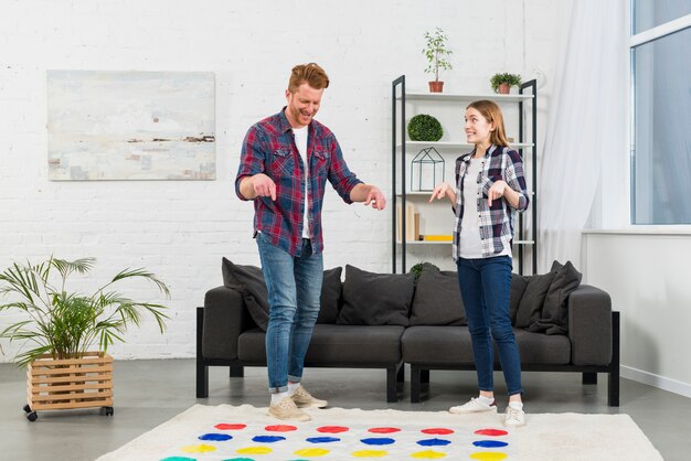 Junge Paare, die den Finger über dem Farbpunktspiel im Wohnzimmer zeigen
